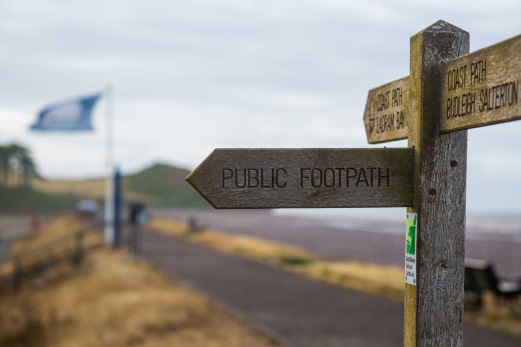 A wooden public footpath waymarker sign with blurred background